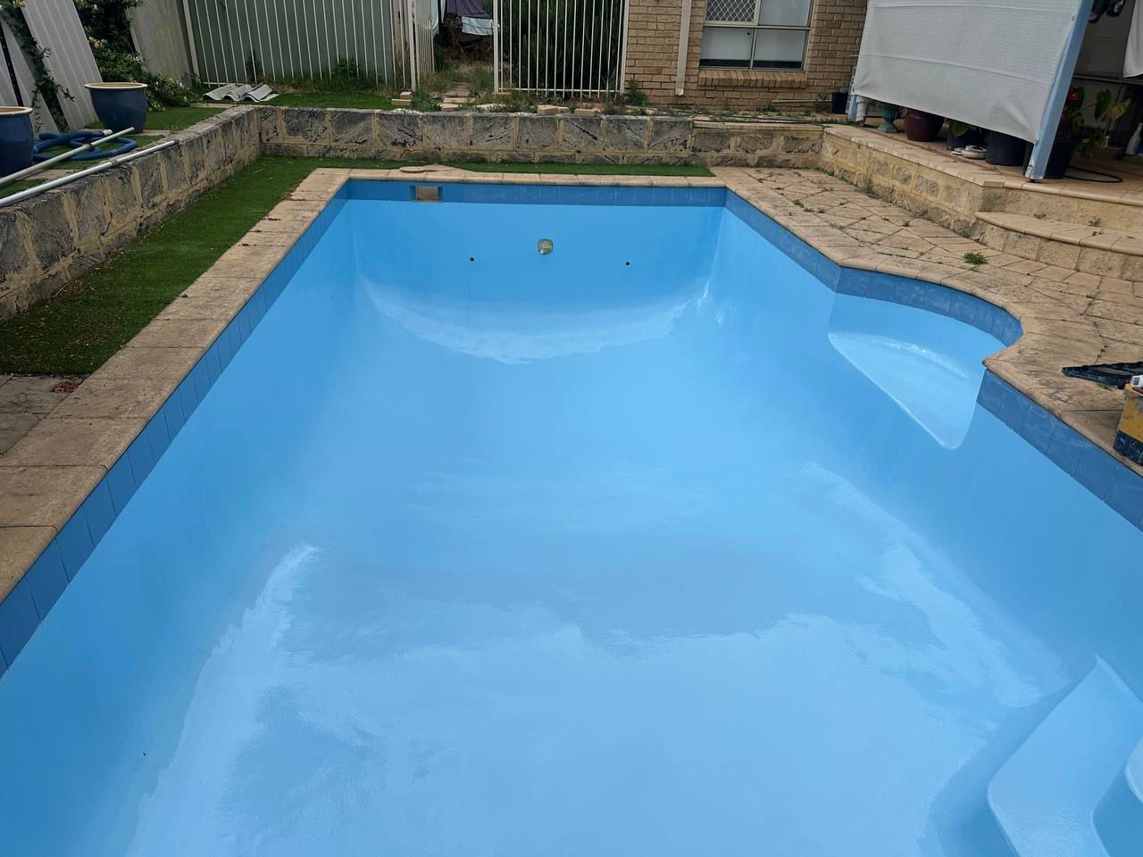 Backyard swimming pool freshly resurfaced in a deep, glossy blue coating